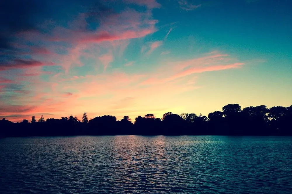 Sunset over a calm lake with a dark line of trees in Babylon, New York