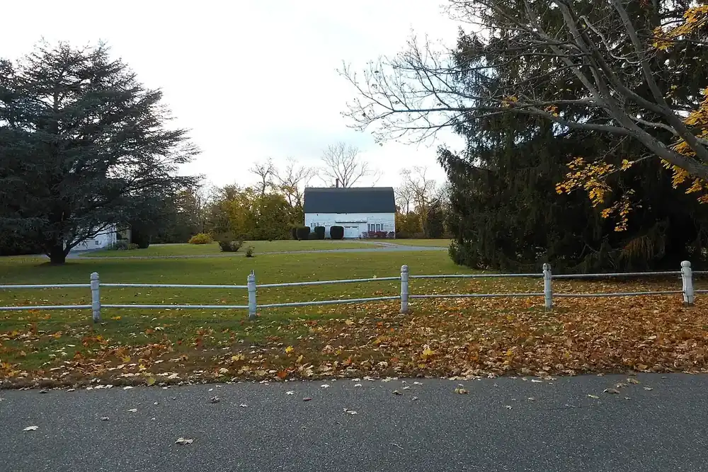 Open lawn with a white rail fence and autumn trees in Bay Shore, New York
