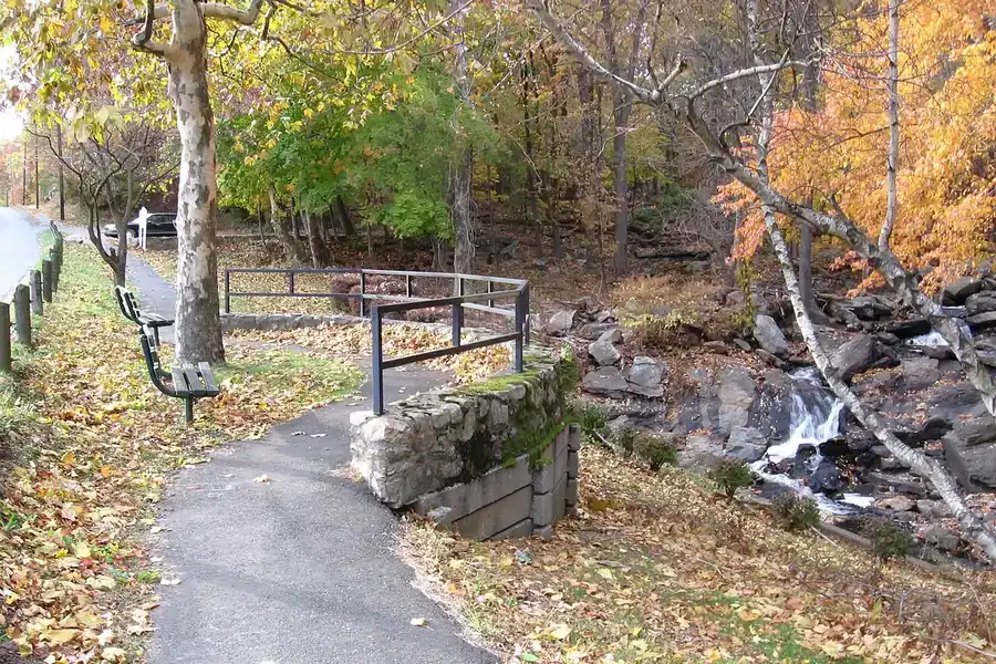 Paved park path beside a small stream and autumn trees in Darien, Connecticut