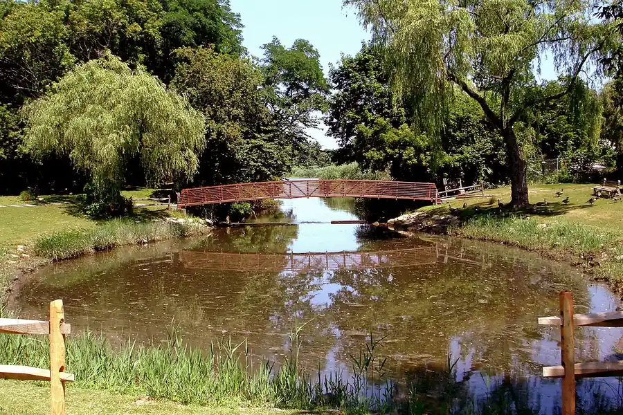 Small red footbridge over a pond among willows in a park in East Setauket, New York