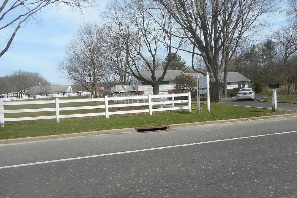 White rail fence along a country road with barns and bare trees in Melville, New York