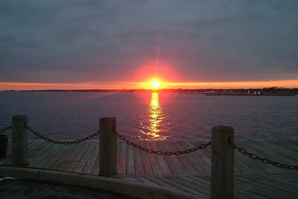 Sun setting over the Great South Bay beyond a waterfront rope fence in Patchogue, New York