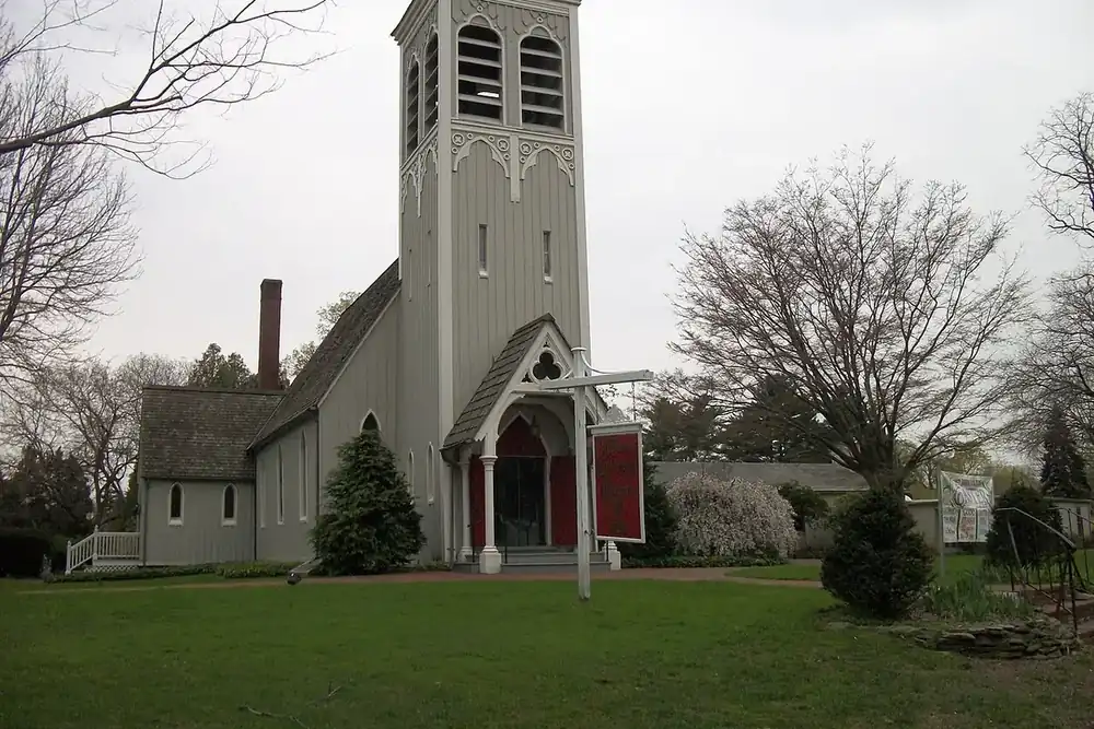 White wooden church with a square bell tower on a green lawn in St. James, New York