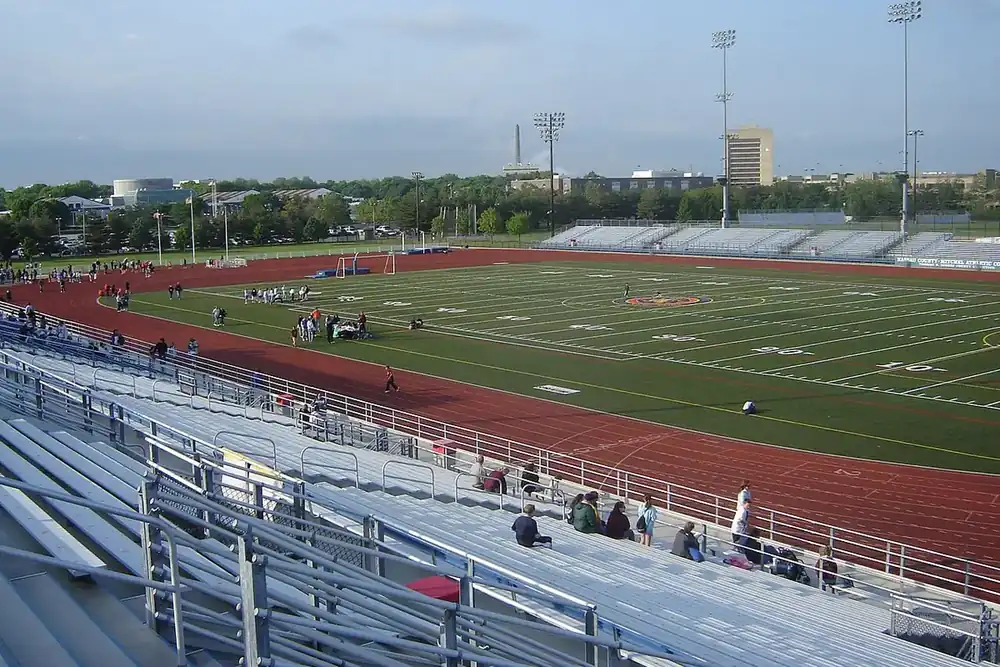 Red running track and green athletic field with stands under a clear sky in Uniondale, New York